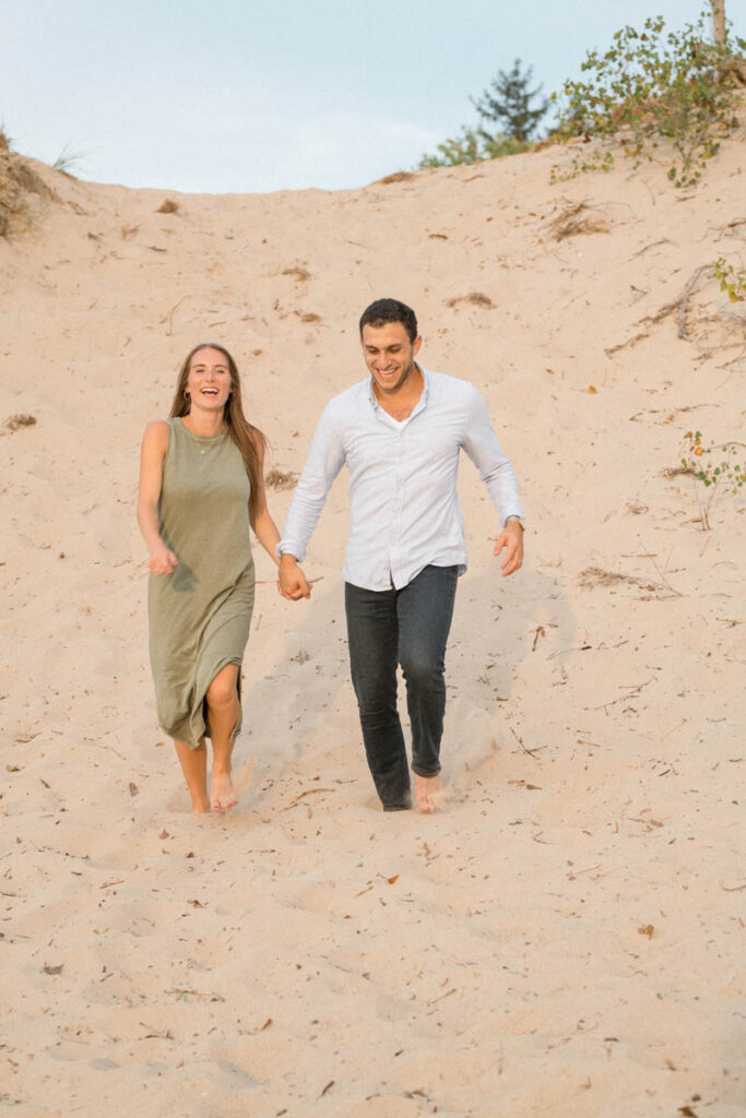 Couple laughs as they run down a large sand dune at Indiana Dunes.