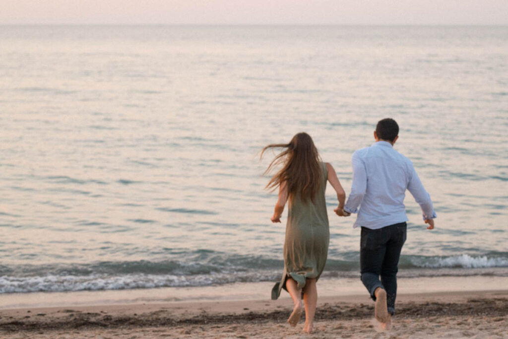 Couple running to water while holding hands on the beach.