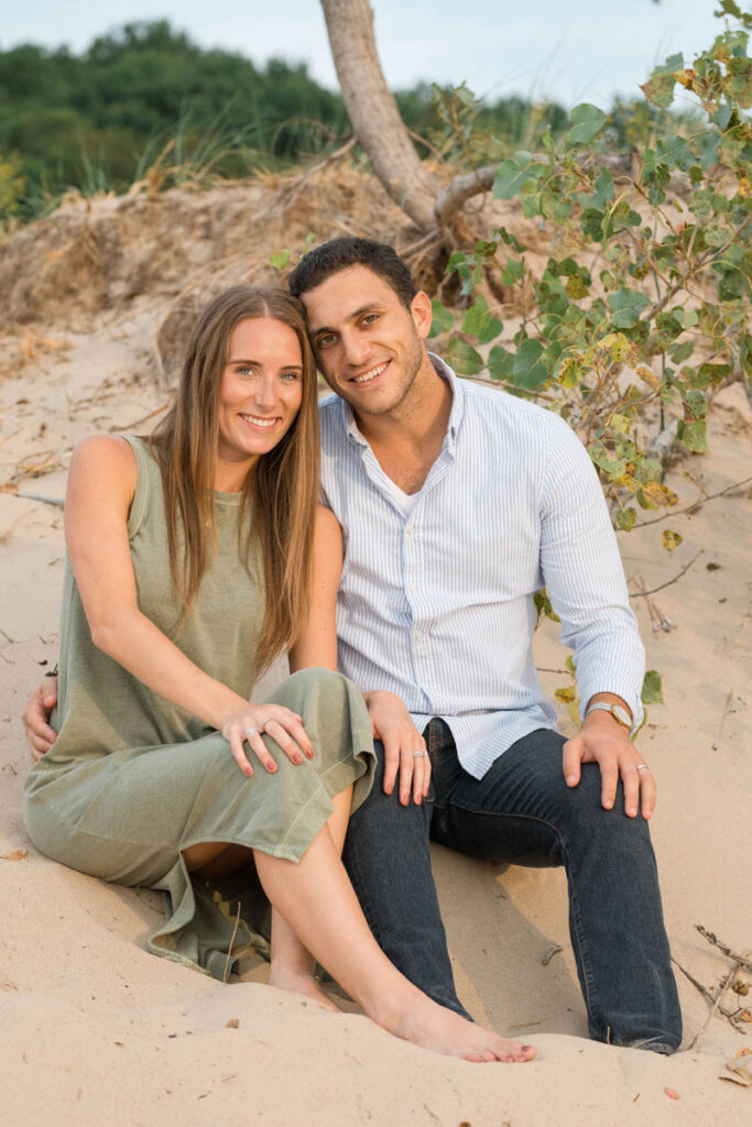Couple smiles while sitting on a sand dune at Indiana Dunes State Park.