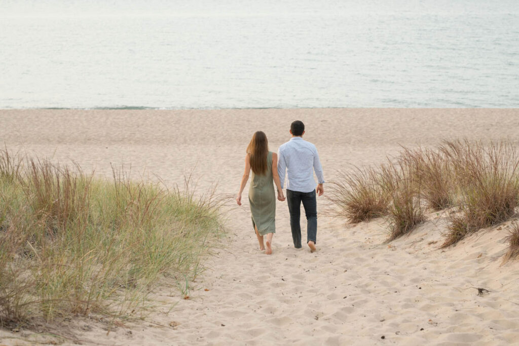 Couple holds hands while walking towards Lake Michigan shoreline.