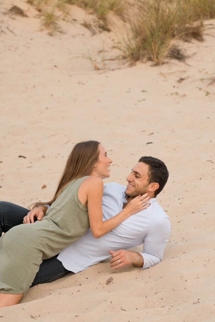Woman laughs while laying in sand with man.