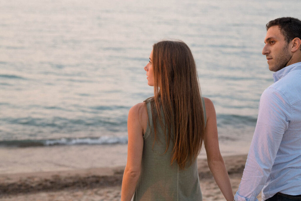 Man and woman look out at the water during their beach couples photography session.