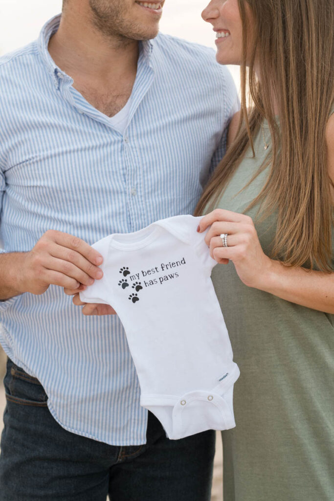 Couples smiles while holding a onesie that says "my best friend has paws."