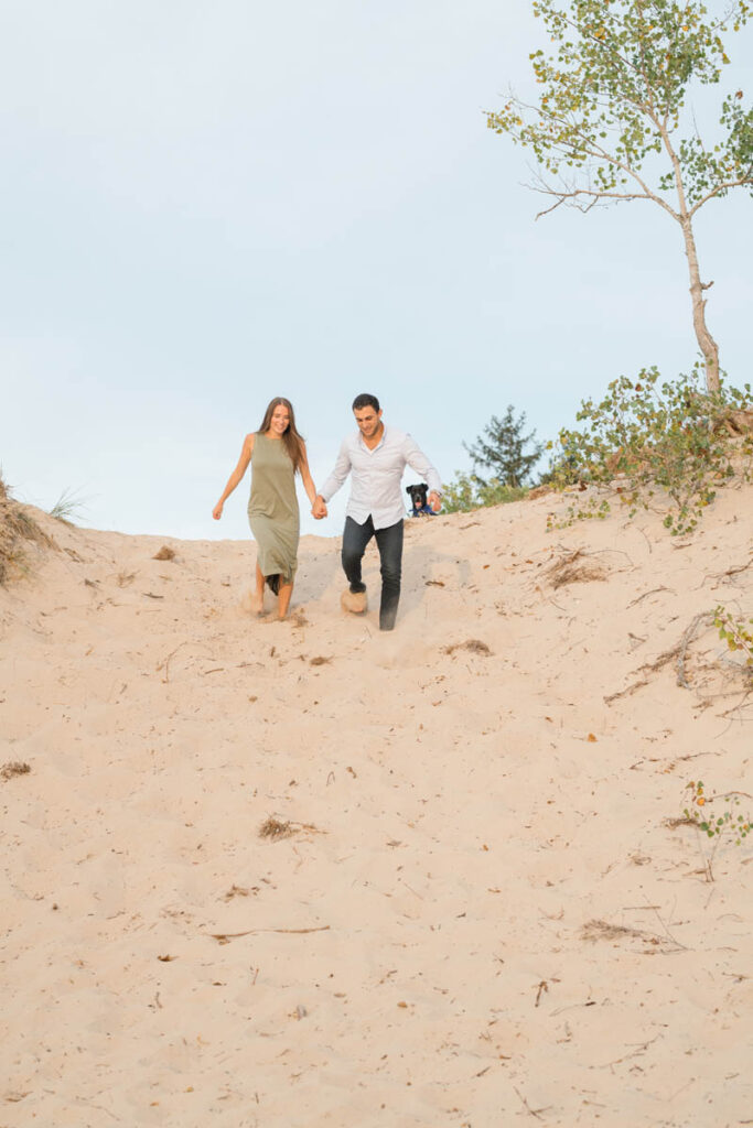 Couple running down a sand dune while holding hands.