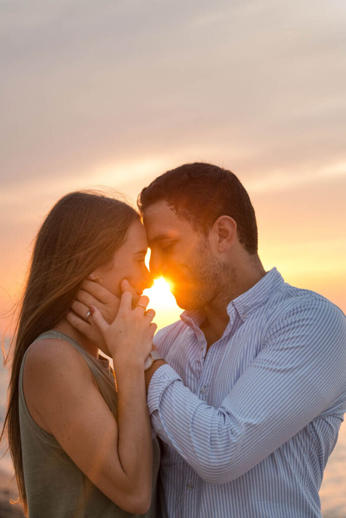 Couple resting heads together with sun shining through during beach couples photography session.