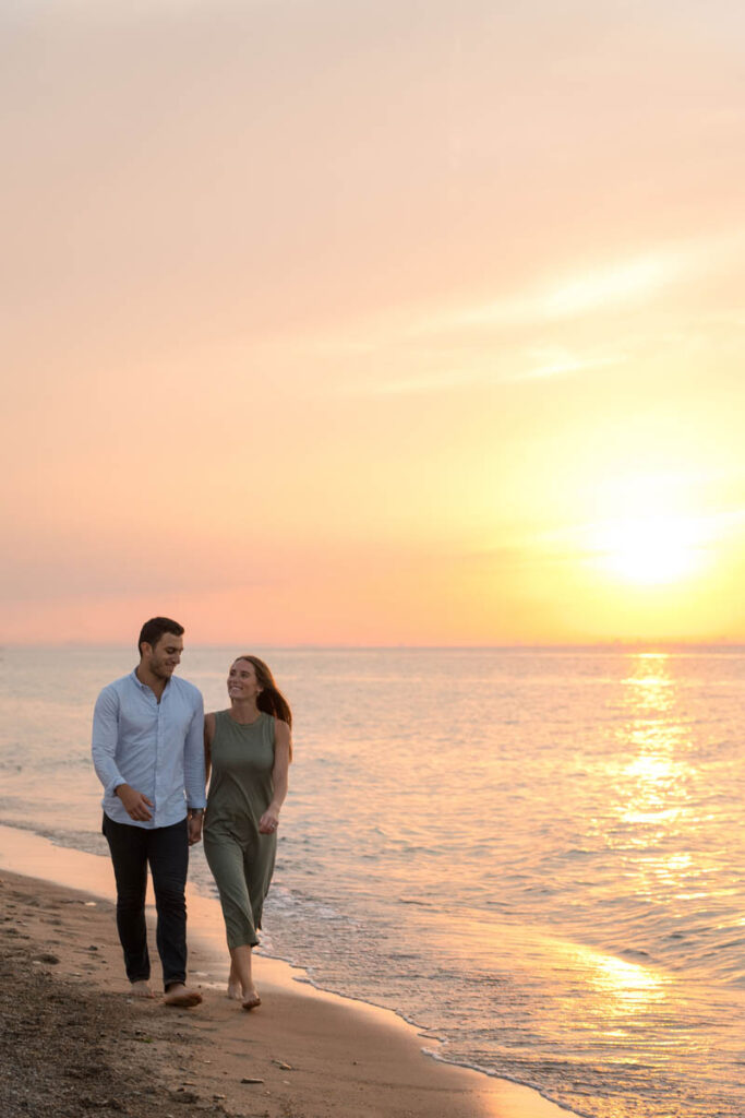 Couple walks along the beach holding hands at sunset.