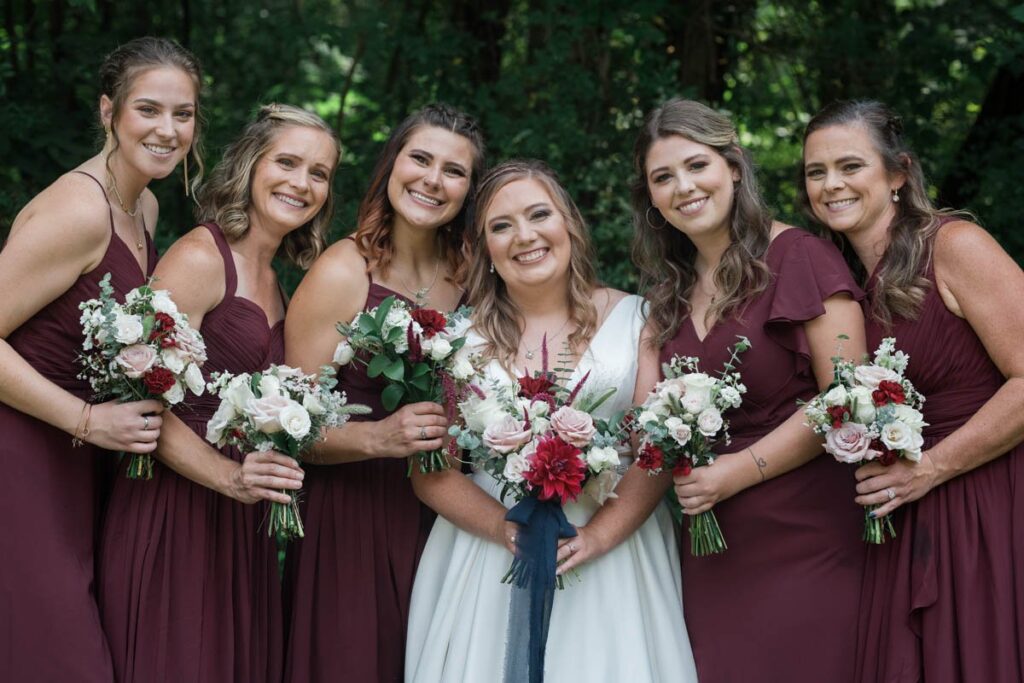 Bride and bridesmaids smile while holding their bouquets.