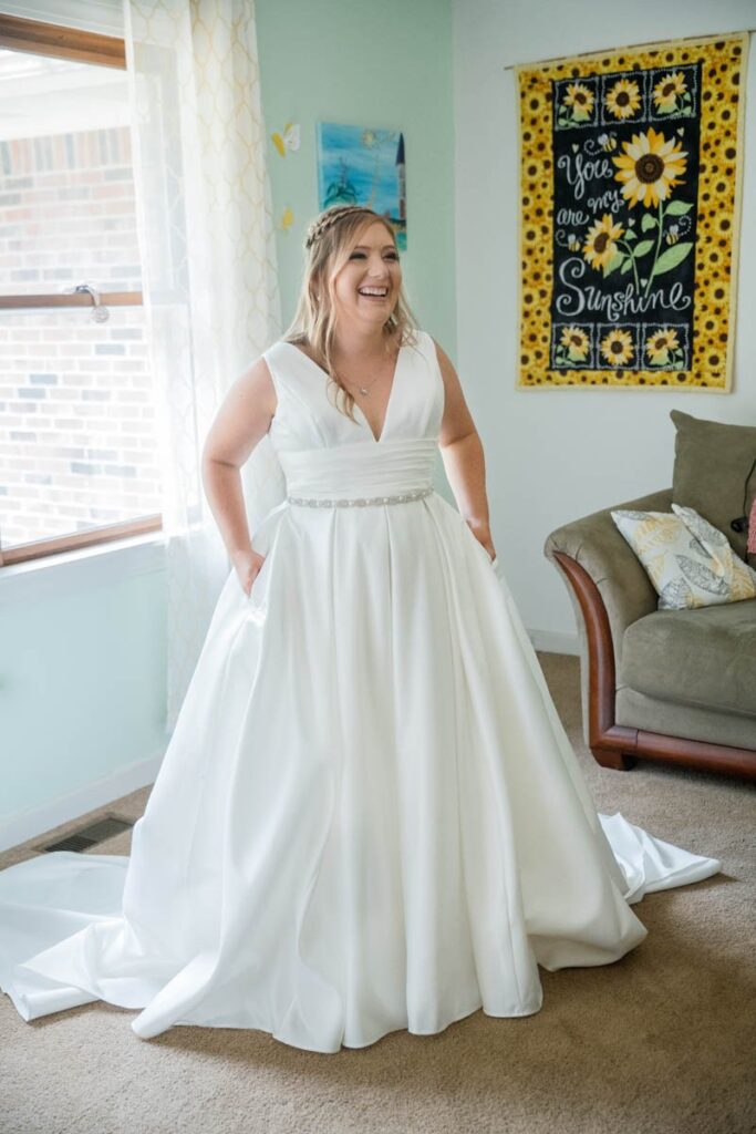 Bride laughs with her hands in the pockets of her wedding dress.
