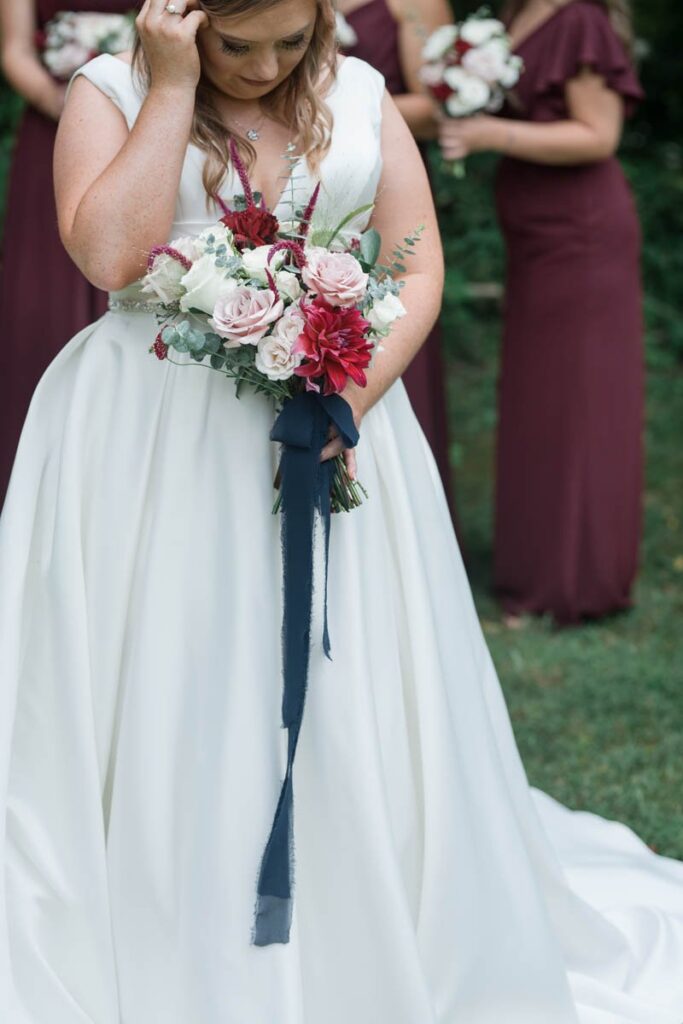 Bride fixes her hair while looking down at her bouquet.