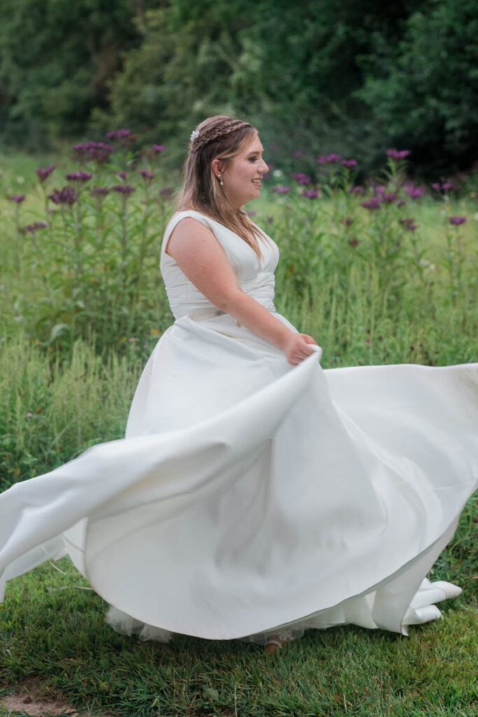 Bride is twirling in her wedding dress with purple wildflowers in the meadow behind her.