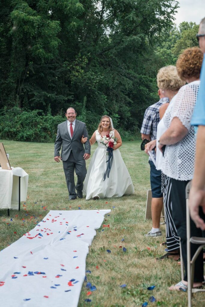 Bride's father walks her down the aisle during outdoor wedding ceremony.