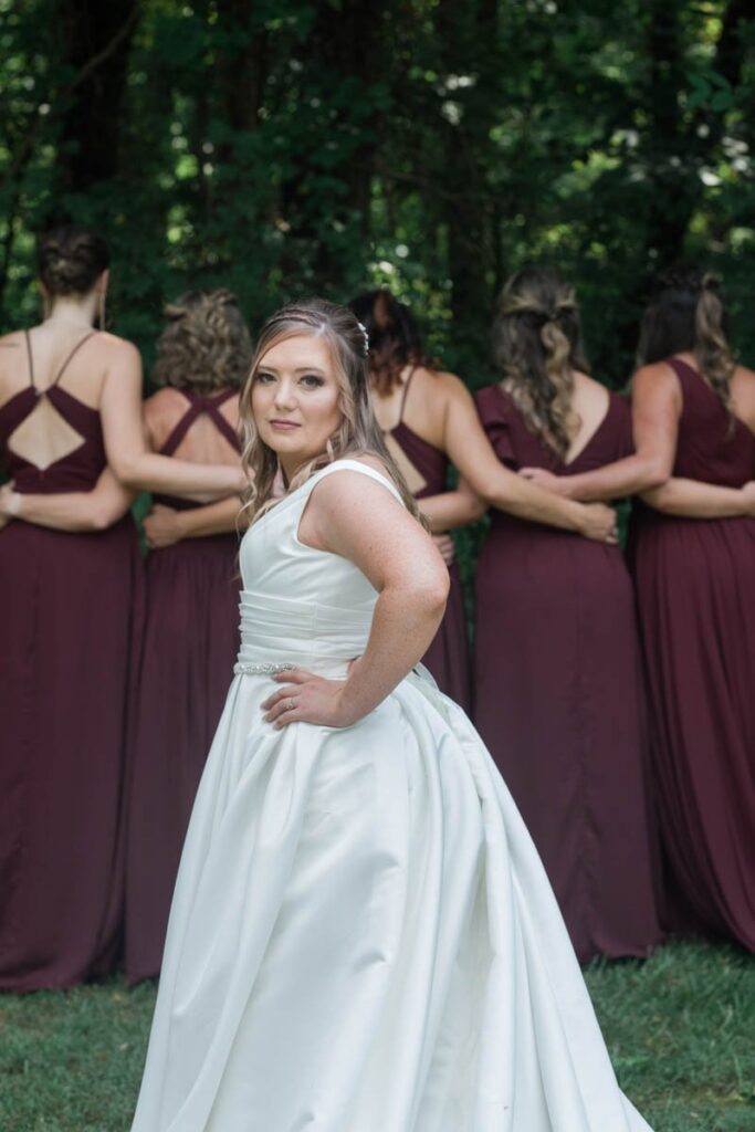 Bride stands in front of bridesmaids with her hand on her hip.
