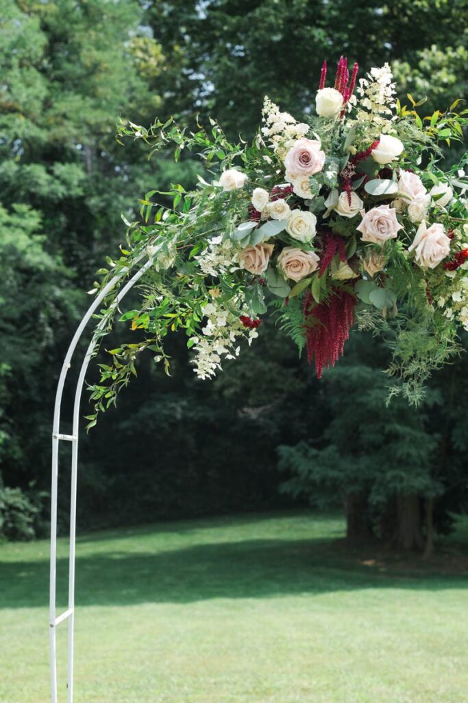 Blush, red, and white flowers with greenery on wedding arch.
