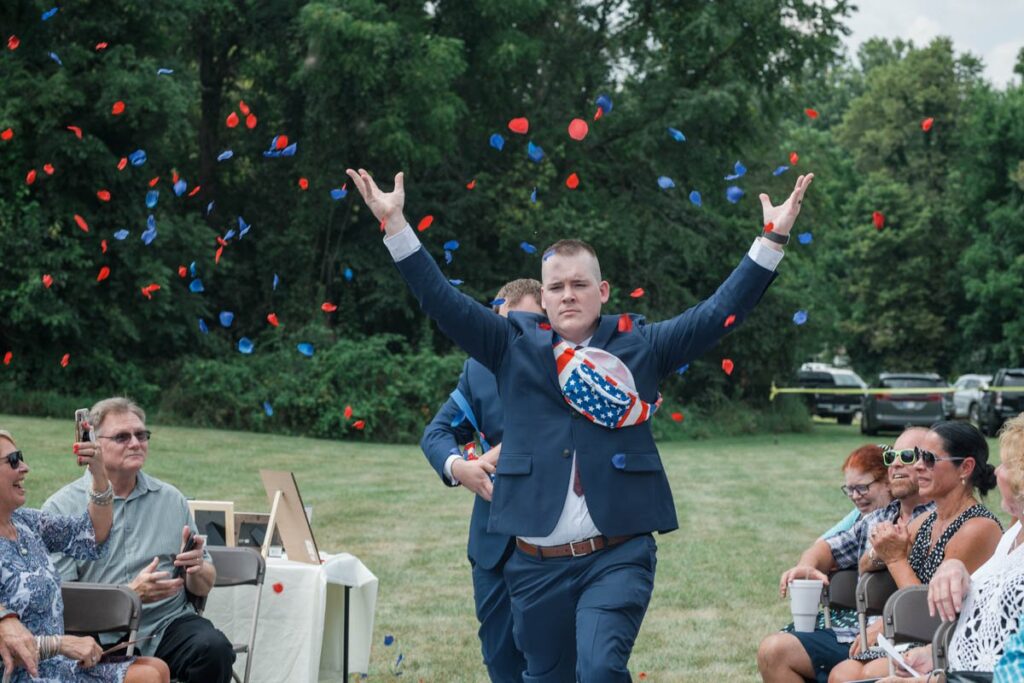 Flower men throw red and navy petals out of fanny packs while walking down the aisle.