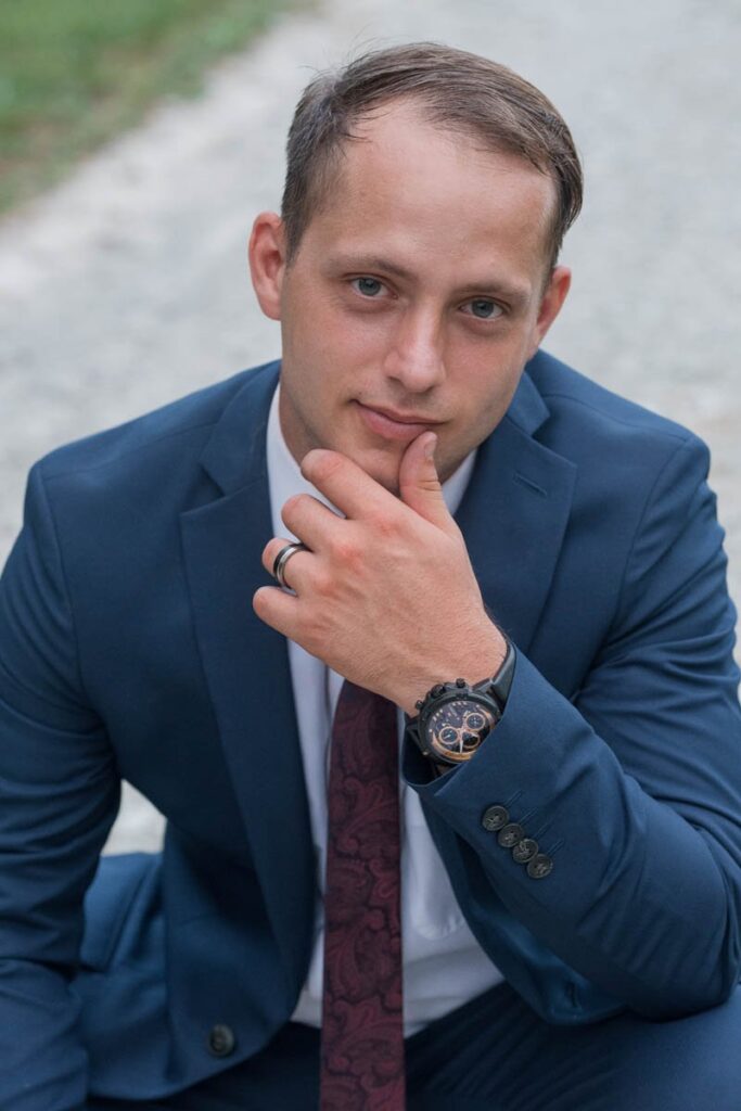 Groom is crouching down with his hand on his chin showing his wedding band.