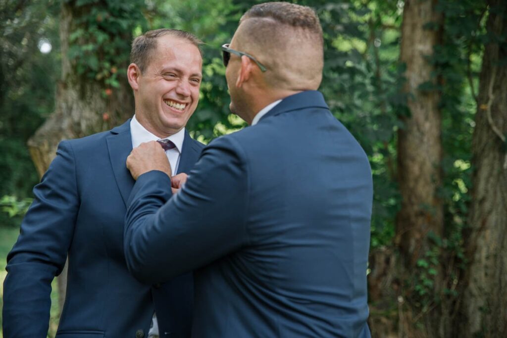 Groom is laughing while his brother fixes his tie.