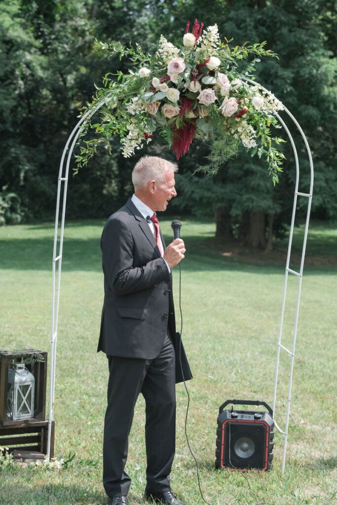Officiant speaks into microphone during outdoor wedding ceremony.