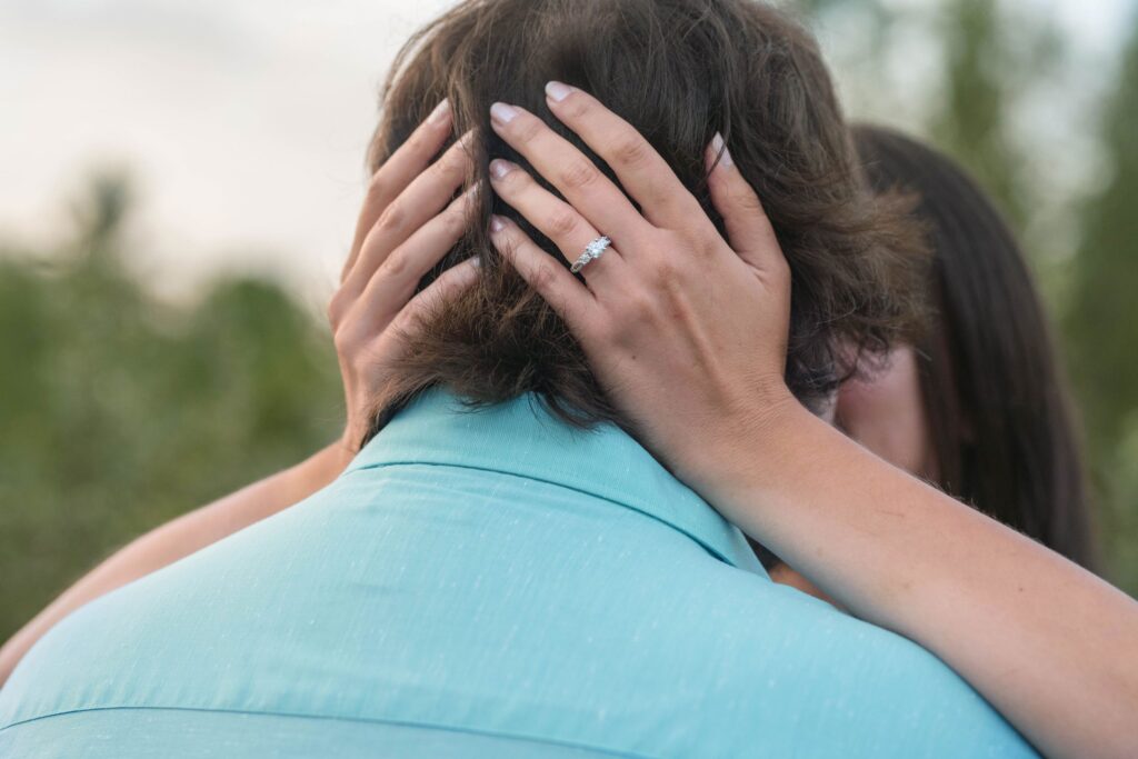 Woman wearing engagement ring put hands on the back of man's head.