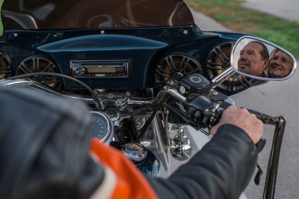 Couple's faces reflect in Harley rearview mirror as they sit on the bike.