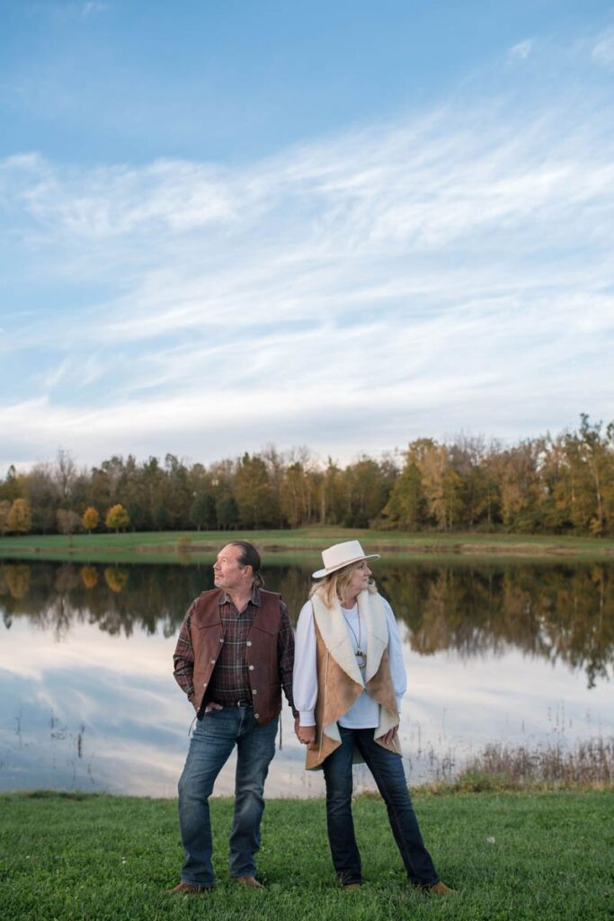 Couple holds hands while looking in opposite directions in front of a reflective lake during their couples photography session.