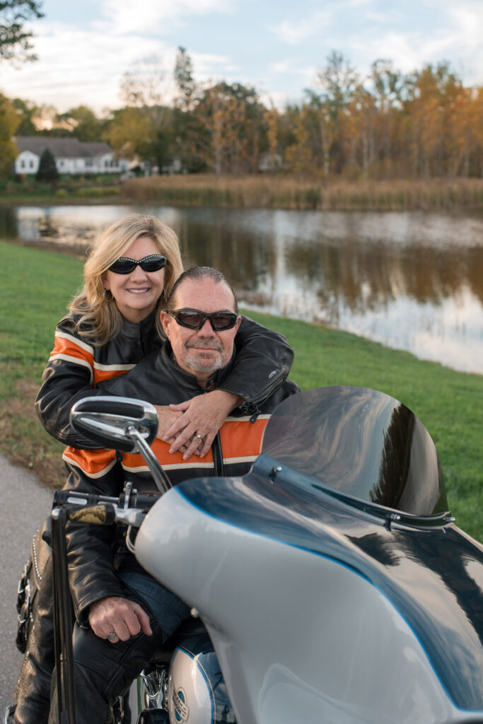 Woman has arms around man as they sit on Harley.