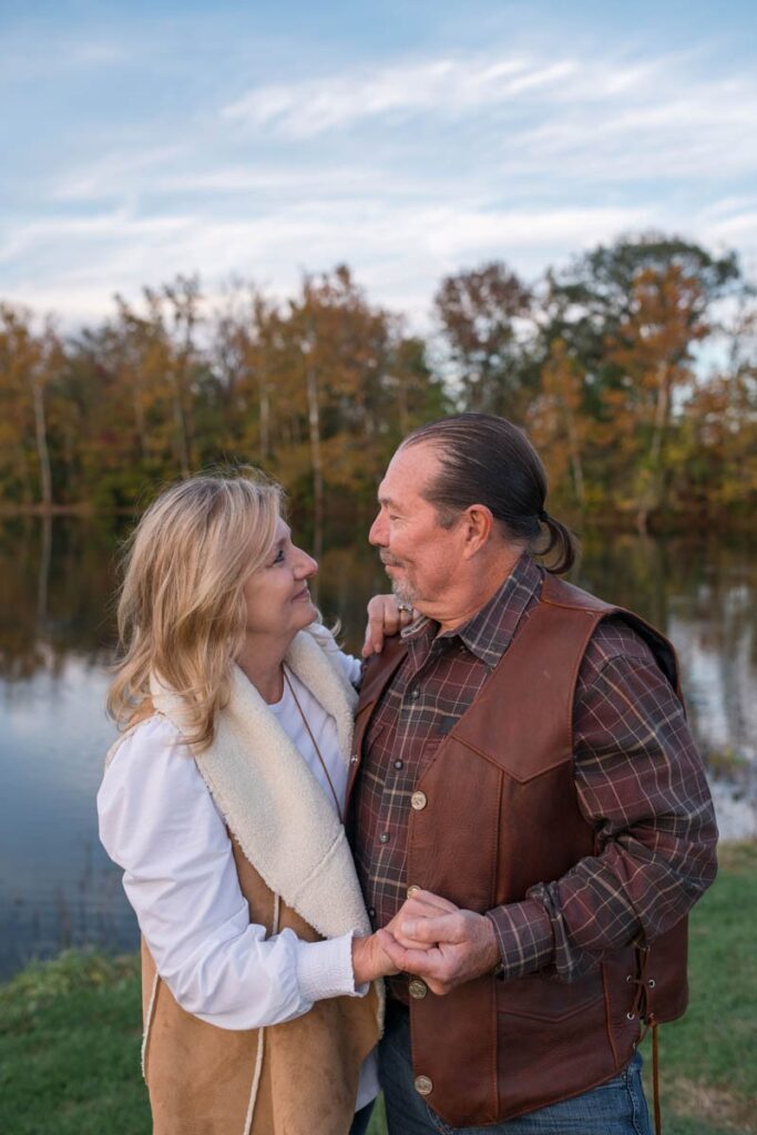 Husband and wife hold hands with arms around each other looking at one another happily.