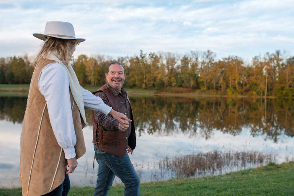 Man smiles while holding woman's hand and leading her on a walk.