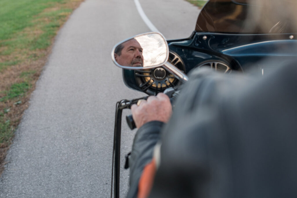 Man's face reflects in Harley's mirror as he sits on bike.