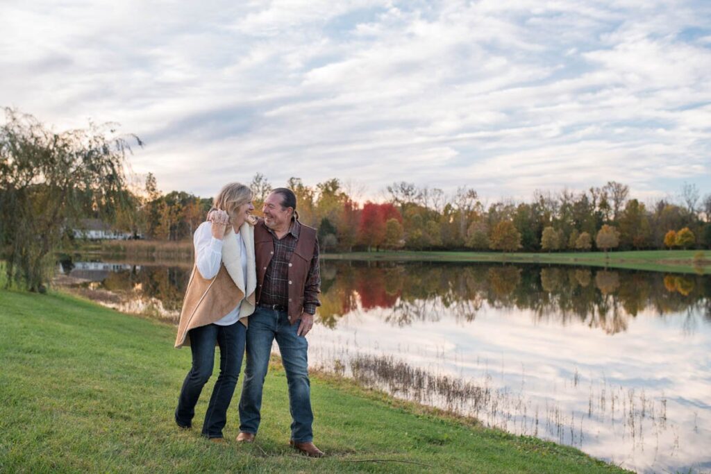 Couple walks along lakeside during fall under a blue sky.