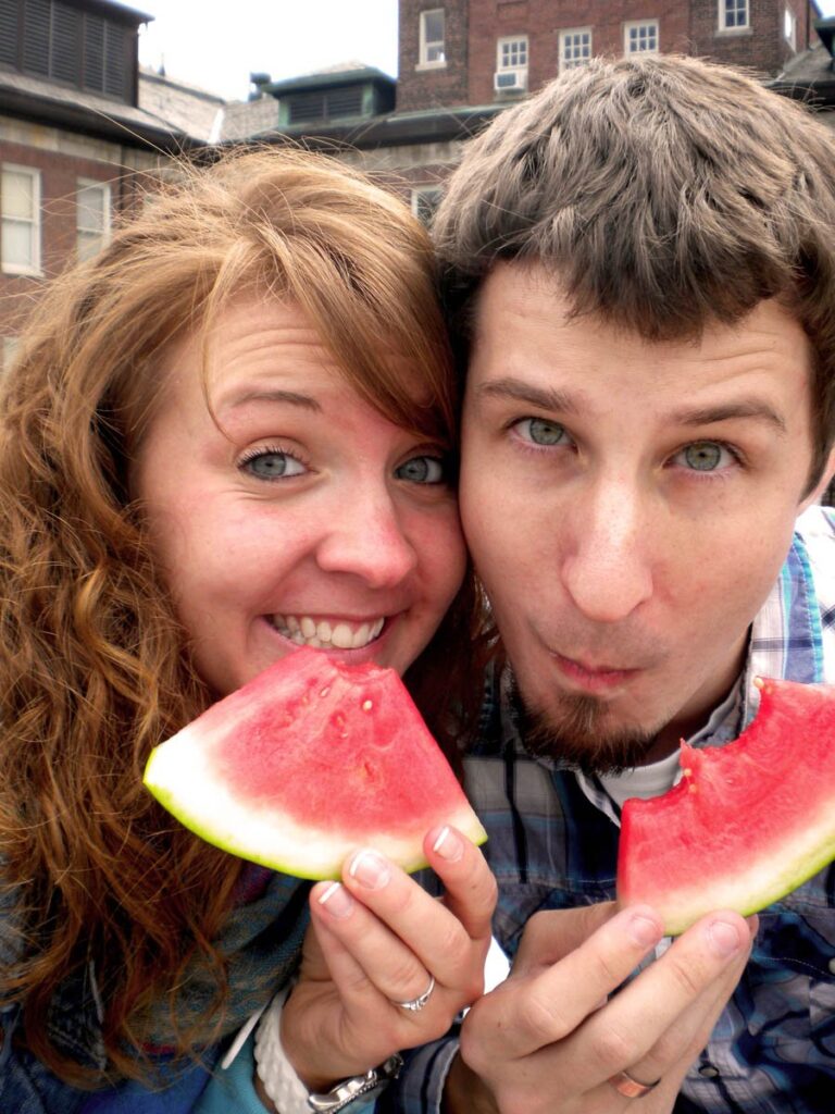A couple makes silly faces while eating watermelon.