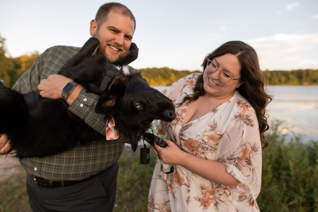 Couple holds dog upside dog while smiling and petting him.
