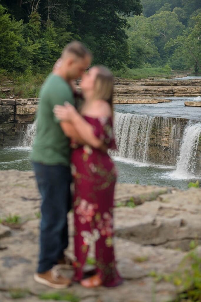 Couple embraces while the waterfall behind them is in focus.