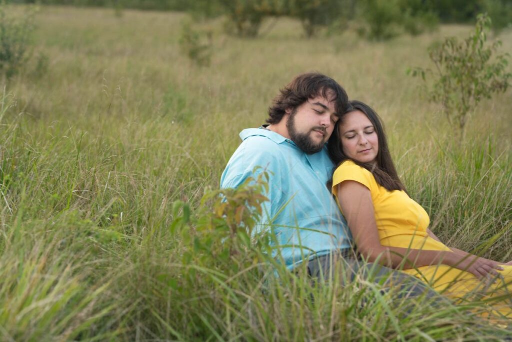 Couple closes their eyes and rests against each other in a meadow.