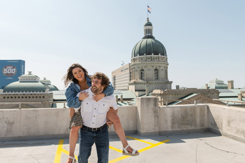 Couple laughing during piggy back ride on parking garage roof.
