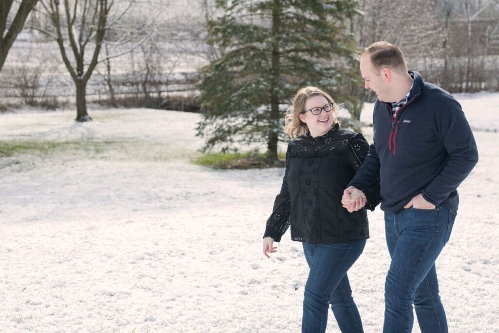 A couple holds hands while walking through the snow together.