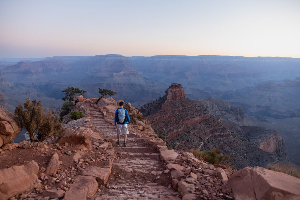 Man hikes along trail at Grand Canyon National Park at sunrise.