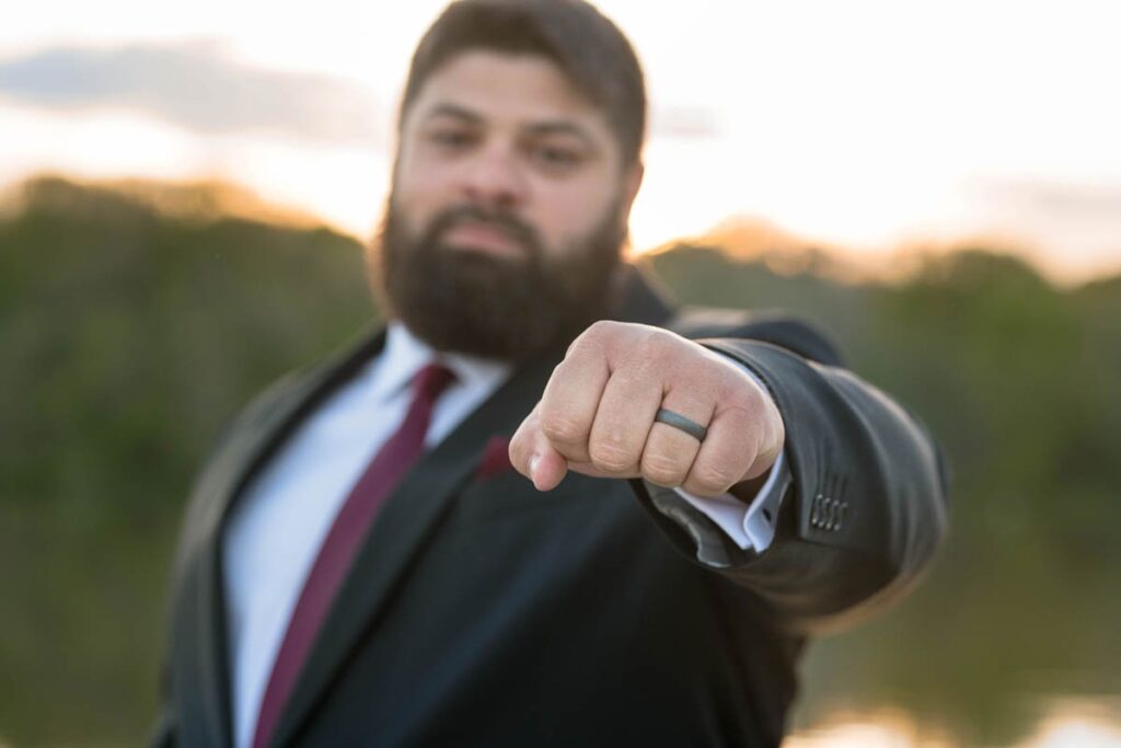 Groom is showing off his wedding band by sticking out his fist in front of him.