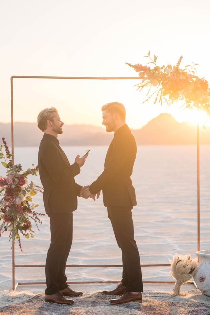Grooms are holding hands and reading vows at sunset in the Bonneville Salt Flats in Utah.