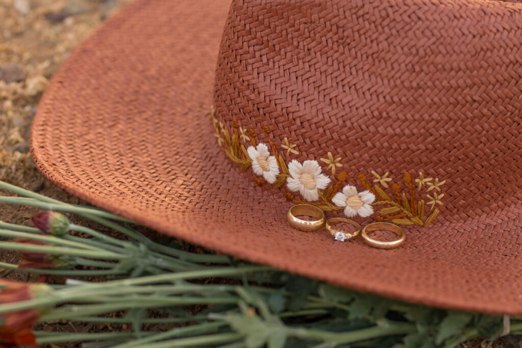 Wedding rings sit on rust-colored hat with embroidered flowers.
