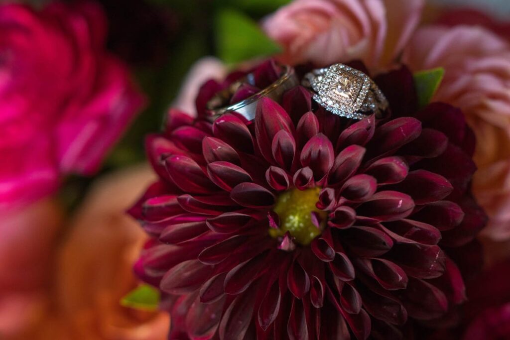 Wedding rings rest on top of a maroon flower on bride's wedding bouquet.