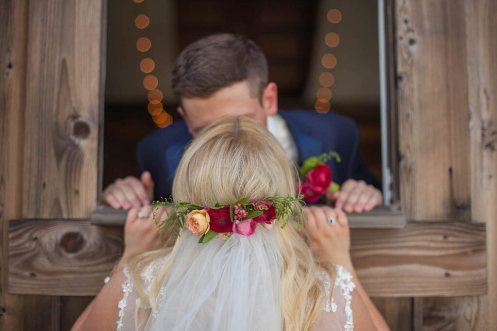Bride kisses groom through barn window.