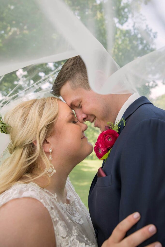 Bride and groom rest their heads together as they smile under bride's veil.