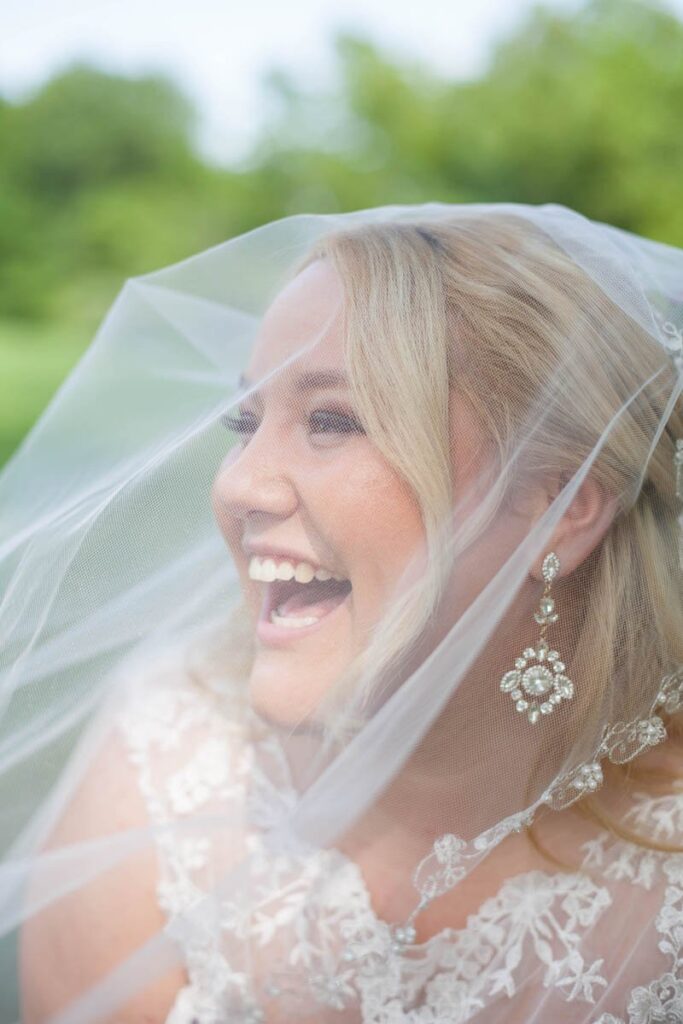 Bride laughs and looks to the left with veil over her face.