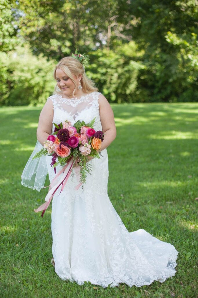 Bride holds bouquet and looks down over her shoulder towards the grass.