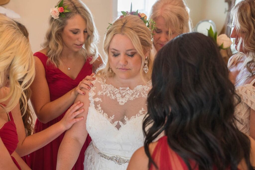Bridesmaids put hands on bride and pray for her.