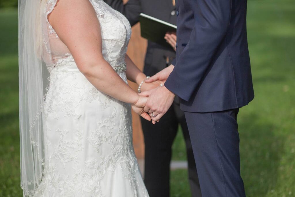 Bride and groom hold hands during outdoor wedding ceremony.