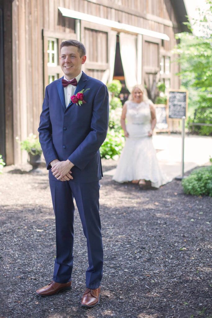 Bride begins walking up to groom during first look outside of barn.