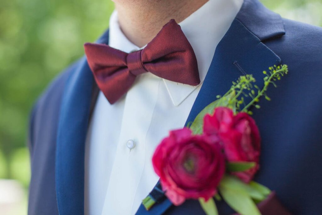 Groom's maroon bowtie and brightly colored boutonniere against navy suit.