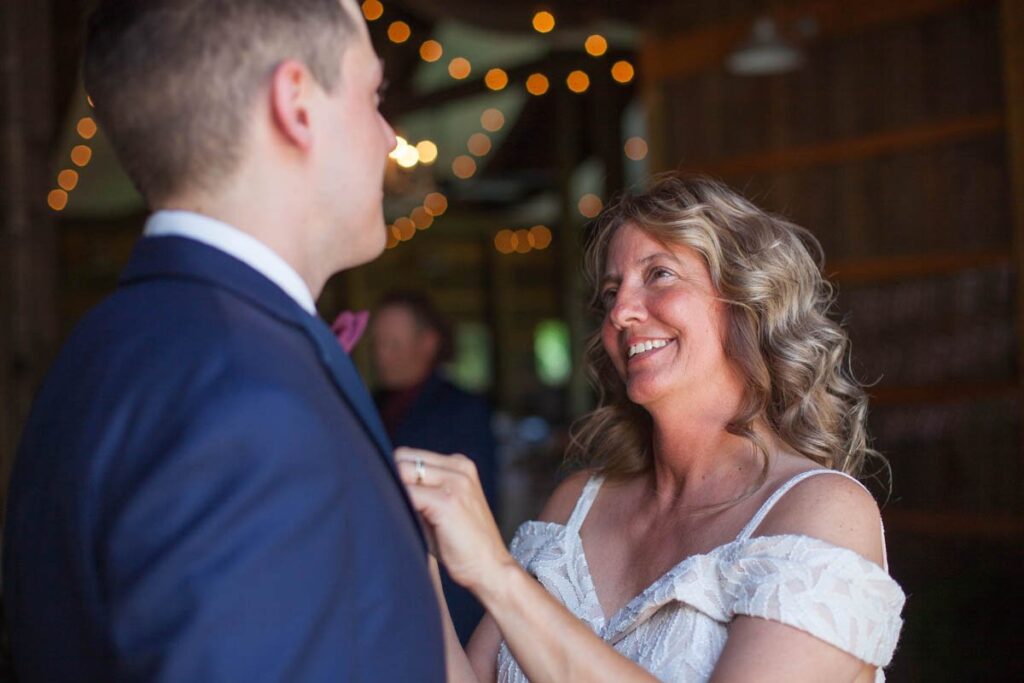 Mother of groom smiles at him as she helps pin his boutonniere.