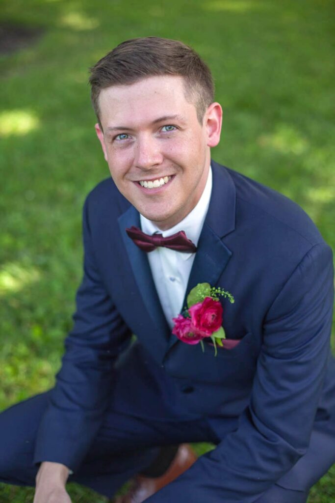 Groom squats down in the grass while smiling.